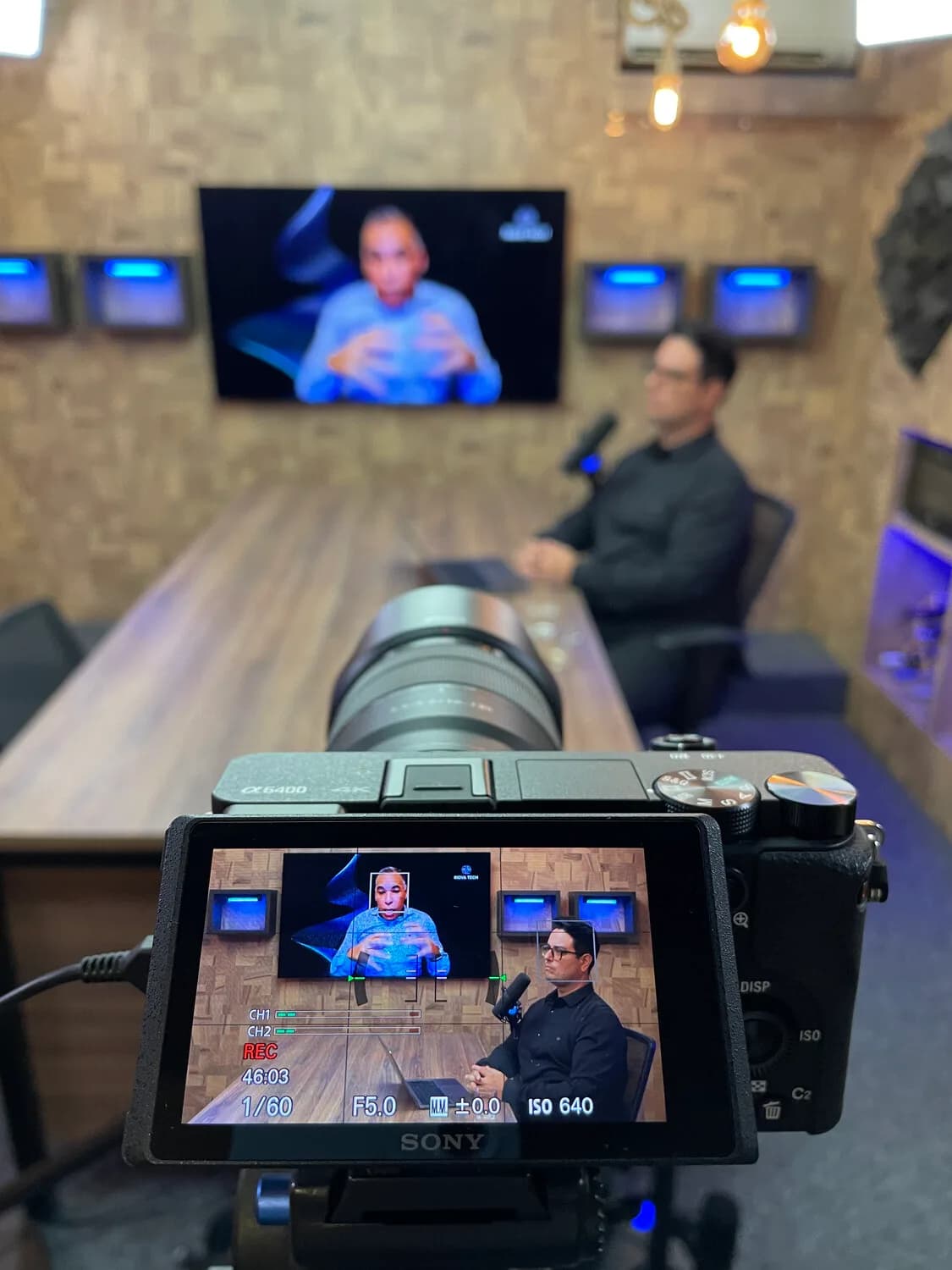 Câmera Sony em primeiro plano com Joás Andrade desfocado ao fundo na tela